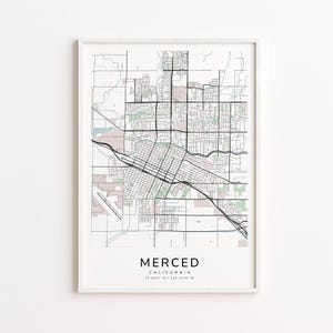 May include: A framed map print of Merced, California, featuring a detailed street layout in black lines against a neutral background. The city name and coordinates are printed in a clean, modern font at the bottom. The frame is white.