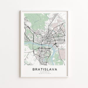 May include: A framed map print of Bratislava, Slovakia, featuring a detailed street layout in black lines against a light background with green and beige accents. The city name is printed in a bold, sans-serif font at the bottom.