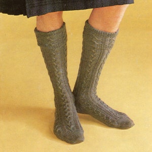 Puede incluir: Calcetines altos hasta la rodilla de punto de cable verde oliva. Los calcetines presentan un puño acanalado y un patrón de cable detallado. Fabricados con un material suave y texturizado, perfectos para el invierno.