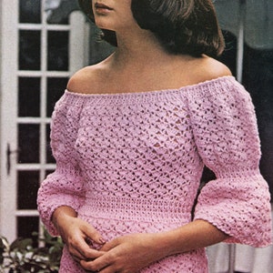 Puede incluir: Un top de ganchillo rosa claro, con hombros descubiertos y mangas tres cuartos. El top tiene una cintura ajustada y un patrón calado. Las mangas se ensanchan en el codo. La modelo lleva una falda blanca.