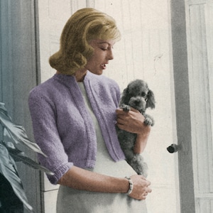 Op de afbeelding: Vintage afbeelding van een vrouw die een lichtpaars vest met korte mouwen draagt over een witte jurk, met een kleine grijze poedel in haar armen. Het vest heeft een ronde halslijn en een geribbelde zoom. De vrouw draagt een armband.