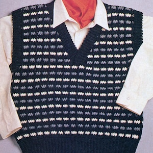 May include: A black crocheted waistcoat with a white and grey pattern. The waistcoat has a V-neck and is shown on a model wearing a white shirt.