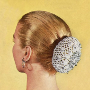 May include: A white crocheted hair bun holder with silver beads. The holder is worn in a woman's blonde hair.