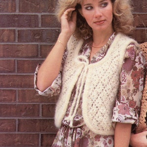 May include: A cream-colored, open-front vest with a delicate, openwork design. The vest has a soft, fuzzy texture and a tie closure. The image also shows a floral print dress and the text "Cissy".