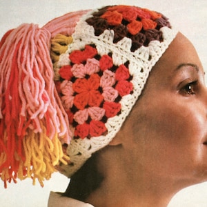May include: A colorful crochet hat with a granny square design in shades of red, orange, pink, and brown. The hat features a white border and a side accent of long, fringed yarn in yellow, orange, and pink. This handmade hat is a unique fashion accessory.