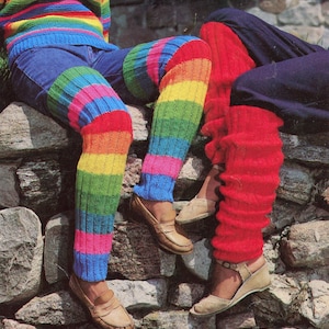 May include: The image features colourful leg warmers in a rainbow pattern, worn with jeans and shoes. The knitted leg warmers display horizontal stripes of red, orange, yellow, green, blue, and pink. The style is retro and striking.