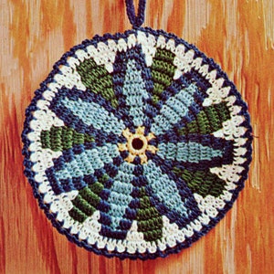 May include: A round, crocheted potholder with a floral design. The potholder features a central yellow circle, surrounded by blue, green, and white geometric patterns. A dark blue loop is attached for hanging. The potholder is approximately 8 inches in diameter.