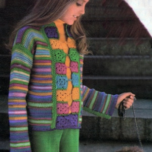May include: A vibrant, crocheted sweater featuring a patchwork design in green, purple, orange, and blue. The sweater has long sleeves and is worn with green trousers. The person is holding a leash.