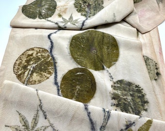 May include: A white fabric with a botanical print of leaves and flowers in shades of green and brown. The fabric is folded and has a textured surface.