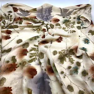 May include: A cream-colored silk scarf with a botanical print featuring brown, green, and gray leaves and flowers.