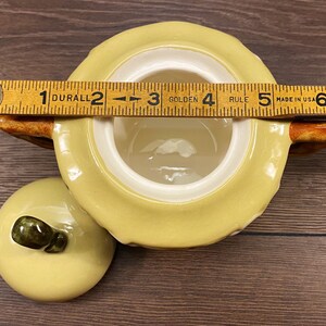 Op de afbeelding: Een gele keramische suikerpot met een deksel en een bruine handgreep. De pot heeft een wit interieur en een getextureerd exterieur. Het deksel heeft een bruine knop. De pot is 12,7 cm breed.