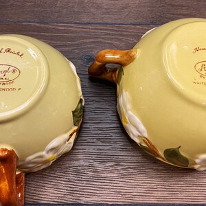 Op de afbeelding: Twee gele keramische kommen met bruine handvatten. De kommen zijn versierd met witte kornoelje bloemen en groene bladeren. De onderkant van de kommen is gemarkeerd met "Handgeschilderd" en "Stangl&reg;  Ovenvast Witte Kornoelje #".
