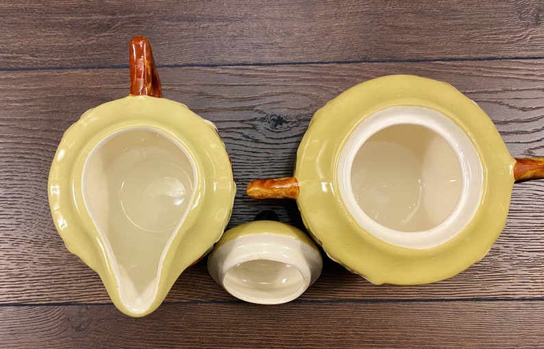 Op de afbeelding: Een set van drie gele keramische theekopjes met bruine handvatten. De kopjes zijn versierd met een bruin en geel patroon.