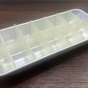 May include: A silver ice cube tray with 12 individual compartments. The tray is empty and ready to be filled with water.