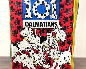 Peut inclure: Un sac à déjeuner 101 Dalmatiens rouge, bleu et jaune avec une fermeture à glissière. Le sac présente un grand logo 101 Dalmatiens et un motif d'empreintes de pattes de dalmatiens. Cinq chiots dalmatiens sont représentés en train de courir sur le devant du sac.