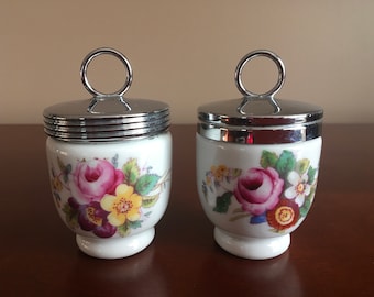 Pode incluir: Dois coqueteleiras de cerâmica branca com desenhos florais e tampas prateadas com alça de anel.