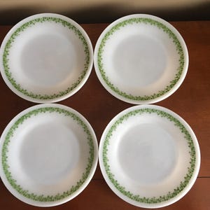 May include: Four white ceramic dinner plates with a green leafy pattern around the edge.