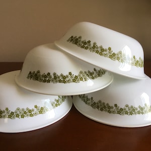 Puede incluir: Cuatro cuencos de cerámica blanca con un patrón floral verde alrededor del borde. Los cuencos están apilados uno encima del otro.