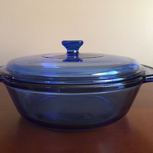 May include: A cobalt blue glass casserole dish with a matching lid. The dish has a rounded shape with two handles and a knob on the lid. This kitchenware is ideal for baking and serving.