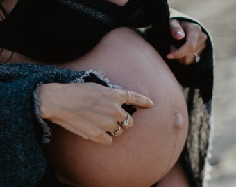 May include: A pregnant person wearing a black bra and a blue and white plaid blanket. The person is touching their stomach with their hand.