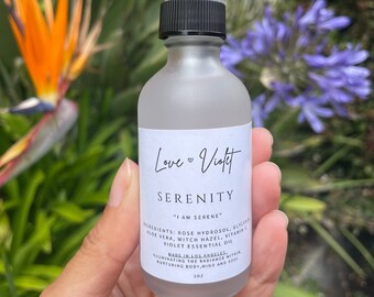 May include: A clear glass bottle with a black spray top and a white label that reads "Love Violet Serenity" and "I am serene". The label also lists the ingredients: Rose Hydrosol, Glycerin, Aloe Vera, Witch Hazel, Vitamin C, Violet Essential Oil. The bottle is made in Los Angeles and is designed to illuminate the radiance within, nurturing body, mind and soul.