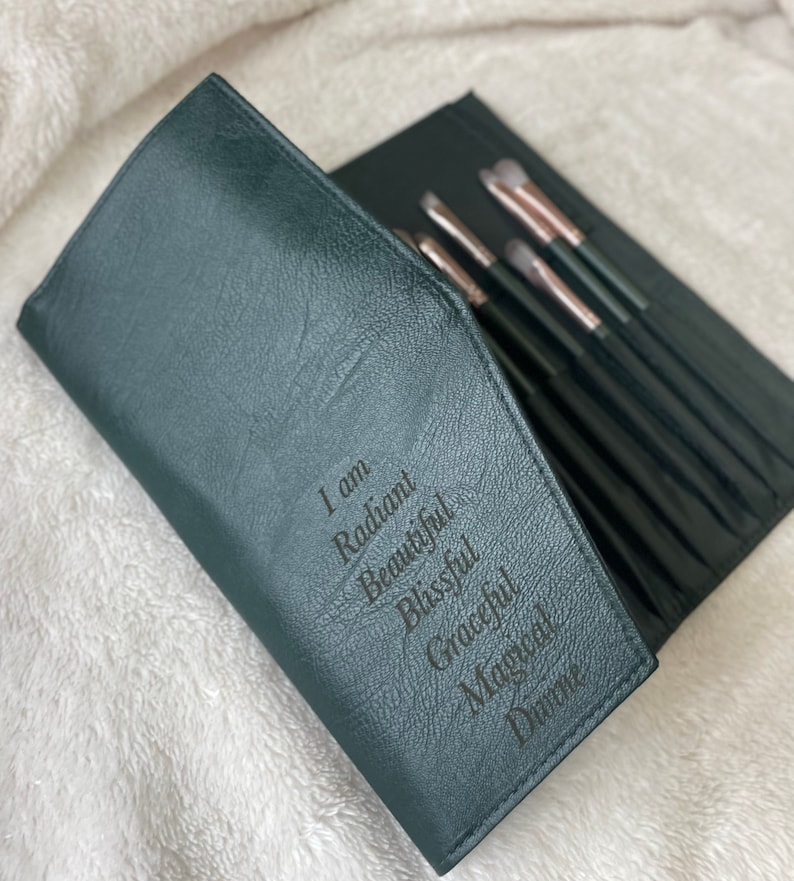 Pu&ograve; includere: Un rotolo per pennelli da trucco in pelle verde scuro con le parole "Io sono Radiosa, Bella, Beata, Graziosa, Magica, Divina" incise sul davanti.