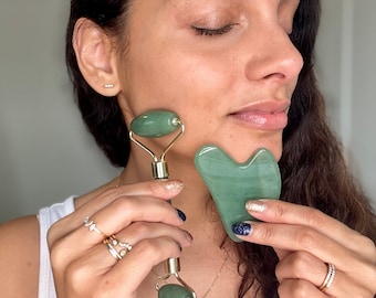 May include: A green jade roller and gua sha tool for facial massage. The roller has a gold handle and two green jade spheres. The gua sha tool is heart-shaped and has a smooth, polished surface.