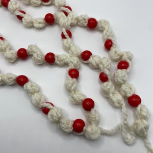 Puede incluir: Una guirnalda blanca de crochet con cuentas rojas. La guirnalda está hecha de hilo y tiene un diseño sencillo. Es perfecta para añadir un toque de alegría navideña a tu hogar.