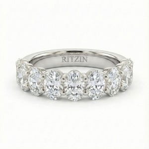May include: A silver band ring featuring seven oval-cut diamonds. The diamonds are set closely together, creating a continuous sparkle. The word "RITZIN" is engraved on the inside of the ring.