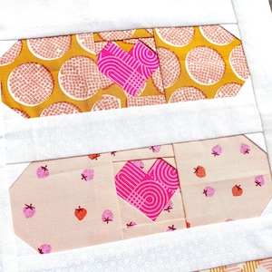 Puede incluir: Primer plano de un diseño de patchwork con tres formas rectangulares y aplicaciones de corazón rosa. El rectángulo superior tiene un fondo amarillo mostaza con círculos blancos. El rectángulo central tiene un fondo rosa claro con patrones de fresas. El rectángulo inferior tiene un patrón de cuadros naranja y blanco.