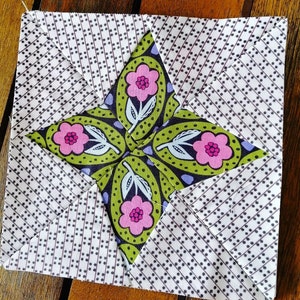 Könnte beinhalten: Ein Patchwork-Quiltblock mit einem Sternmuster. Der Stern ist aus grünem Stoff mit rosa Blumen und Blättern gefertigt. Der Hintergrundstoff ist weiß mit einem schwarz-weißen Tupfenmuster.