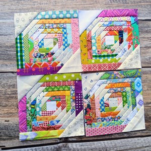 May include: Four square quilt blocks arranged in a grid, each featuring a pineapple log cabin pattern constructed from various colorful fabric strips. The blocks include diverse patterns like polka dots, floral prints, and geometric shapes in bright colors.