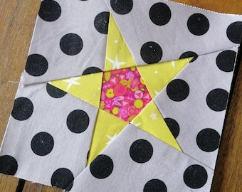 May include: A gray fabric square with black polka dots and a yellow star in the center. The star is made of smaller fabric squares in pink, yellow, and white.