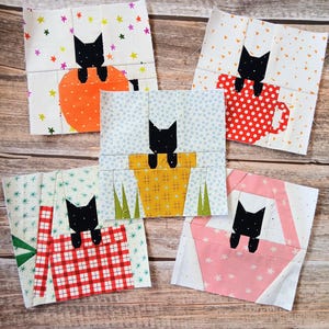 May include: Five square fabric quilt blocks featuring black cat silhouettes. Each block depicts a cat peeking out from different containers: an orange bowl, a red polka-dot mug, a yellow flower pot, a red plaid basket, and a pink basket.