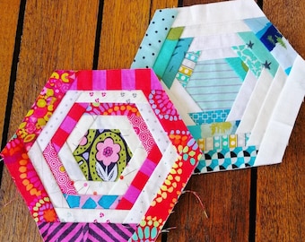 May include: Two hexagonal patchwork quilt blocks, one in pink, red, and white, and the other in blue, white, and green. Both blocks feature a spiral pattern of fabric strips.