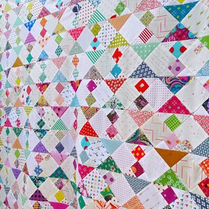 May include: A colorful quilt made of patchwork fabric squares in various patterns and colors, including pink, blue, green, red, and white. The quilt is made up of a repeating pattern of triangles.