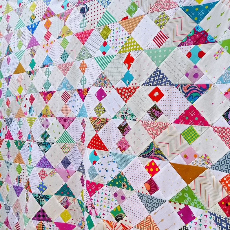 May include: A colorful quilt made of patchwork fabric squares in various patterns and colors, including pink, blue, green, red, and white. The quilt is made up of a repeating pattern of triangles.
