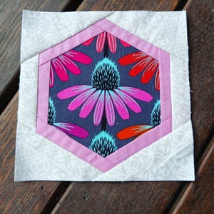 May include: A pink and white fabric hexagon with a floral pattern inside. The hexagon is surrounded by a white fabric with a subtle pattern.