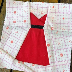 May include: A red dress with a black belt, made from fabric scraps, is being sewn together on a white background with pink sewing symbols.