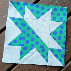 May include: A patchwork quilt block with a white background and green and blue fabric. The green fabric has white polka dots and the blue fabric is solid. The block is made up of triangles and squares.
