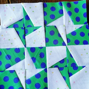 May include: A quilt block with a pattern of alternating white and green squares. The green squares have blue polka dots. The white squares have a small, scattered pattern of yellow, pink, and green squares.