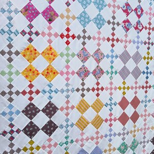 May include: A handmade quilt with a repeating pattern of colorful squares and white blocks. The quilt features various fabrics with floral, polka dot, and geometric designs in shades of pink, blue, yellow, and red.