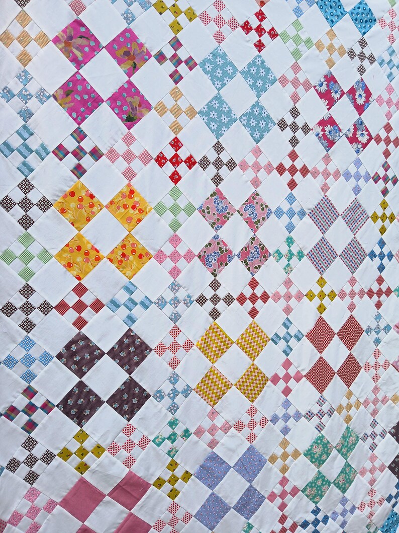 May include: A handmade quilt with a repeating pattern of colorful squares and white blocks. The quilt features various fabrics with floral, polka dot, and geometric designs in shades of pink, blue, yellow, and red.