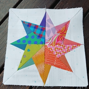 May include: A colorful patchwork star quilt block with eight points. The star is made of different fabrics with geometric patterns in shades of pink, orange, yellow, green, blue, and purple.