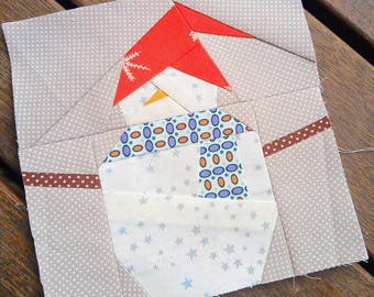 Op de afbeelding: Een handgemaakt stoffen blok met een grillig sneeuwmanontwerp. De sneeuwman heeft een rode hoed, een blauw en oranje patroon sjaal en een witte body met blauwe sterren. De achtergrond is lichtgrijs met witte stippen.
