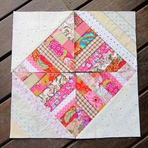 Puede incluir: Un bloque de patchwork compuesto por cuatro secciones. Cada sección presenta un diseño de diamante central con tiras de telas florales, de lunares y estampadas en rosa, rojo y beige. Las esquinas son blancas con lunares rojos.