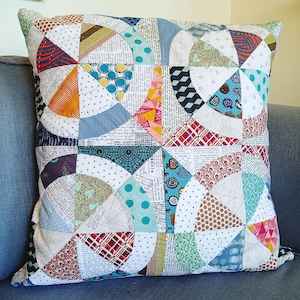 May include: A colourful patchwork cushion with a geometric design featuring circles and arcs in shades of blue, green, red, orange, brown, and white.