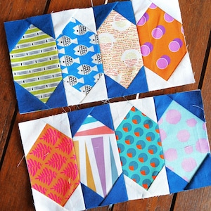 May include: A collection of colorful fabric blocks arranged in two rows. Each block features a unique pattern, including stripes, fish, and polka dots, set against a white and blue background. The blocks are likely for a quilting project.