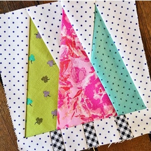 May include: A patchwork quilt block with a geometric design featuring four triangles in green, pink, and blue fabrics. The triangles are sewn together to create a larger triangle shape. The background fabric is white with blue polka dots.