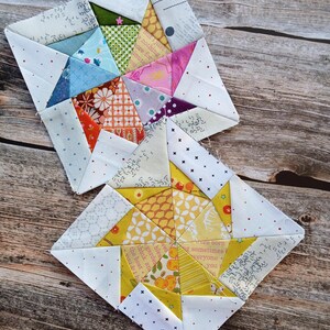 May include: Two square quilt blocks constructed from various cotton fabric scraps. The top block features a mix of blue, green, pink, and orange geometric patterns. The bottom block is primarily yellow with fruit and floral prints, both accented with white fabric.